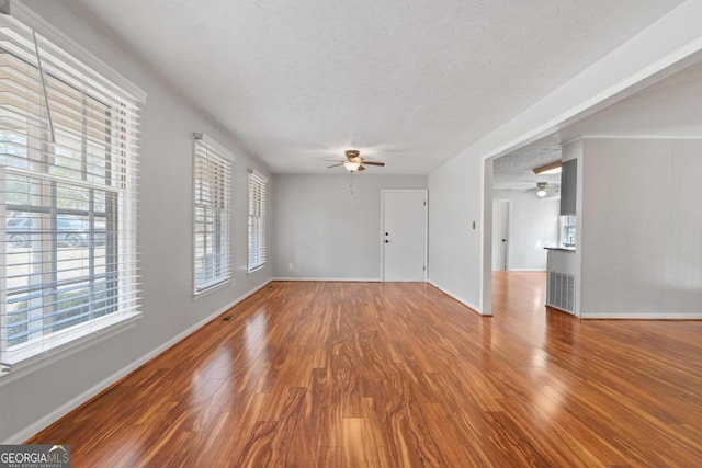 unfurnished living room featuring ceiling fan, a textured ceiling, baseboards, and wood finished floors