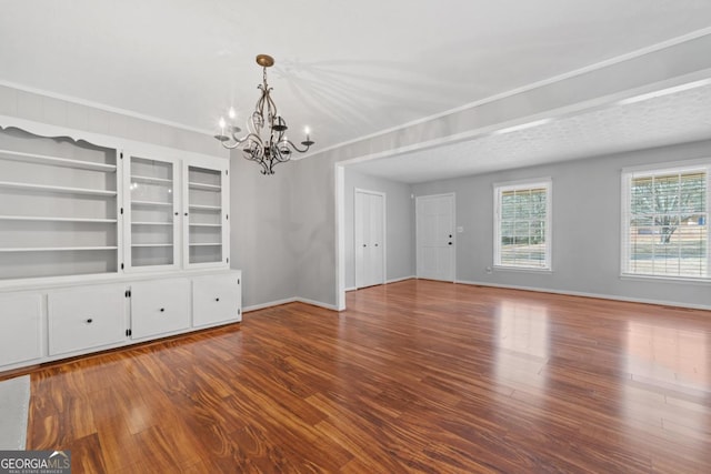 interior space featuring an inviting chandelier, baseboards, wood finished floors, and ornamental molding