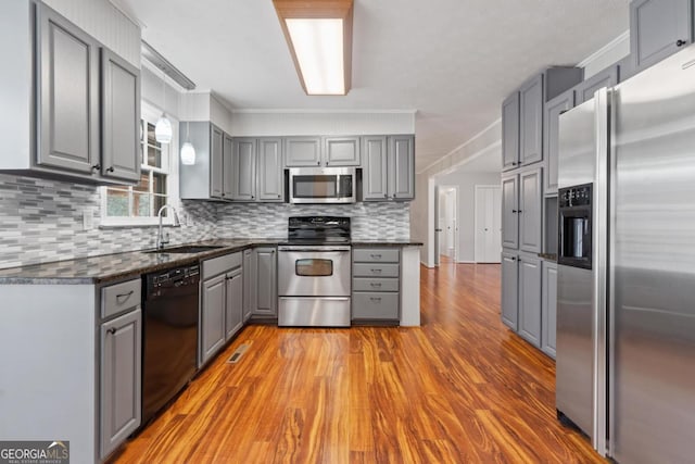 kitchen with stainless steel appliances, a sink, light wood-style floors, gray cabinets, and dark countertops