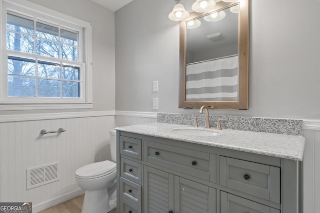 full bath featuring toilet, wood finished floors, vanity, visible vents, and wainscoting