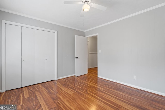 unfurnished bedroom with ceiling fan, wood finished floors, baseboards, a closet, and crown molding