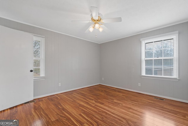 unfurnished room with ceiling fan, wood finished floors, visible vents, and crown molding