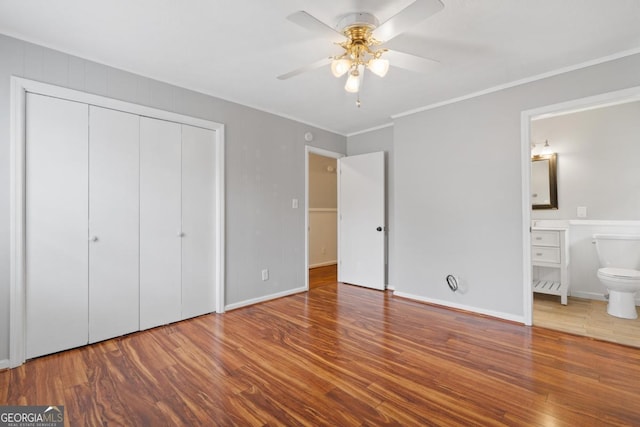 unfurnished bedroom with a closet, ensuite bathroom, ornamental molding, wood finished floors, and baseboards