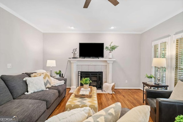 living room with ceiling fan, a tile fireplace, wood finished floors, baseboards, and ornamental molding