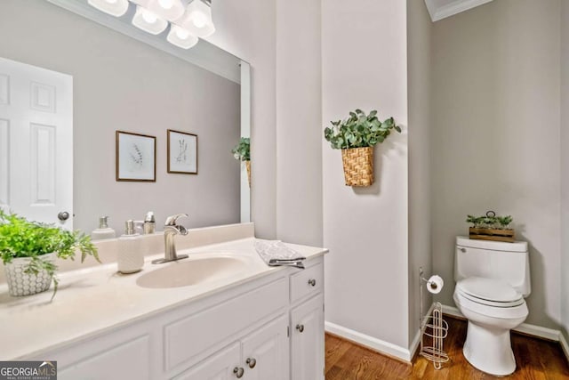 half bathroom with baseboards, vanity, toilet, and wood finished floors