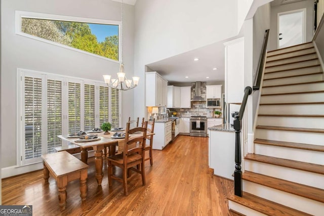 dining space featuring light wood finished floors, a high ceiling, stairway, and a chandelier