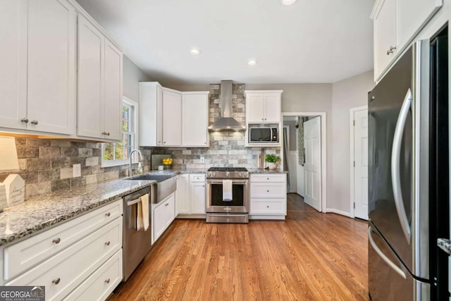 kitchen with a sink, white cabinets, appliances with stainless steel finishes, wall chimney range hood, and tasteful backsplash