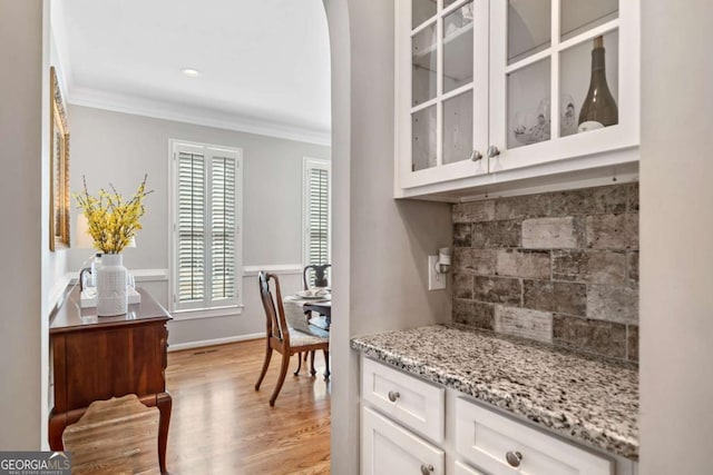 bar with arched walkways, baseboards, ornamental molding, decorative backsplash, and light wood finished floors