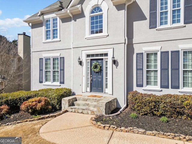 entrance to property featuring a shingled roof and stucco siding