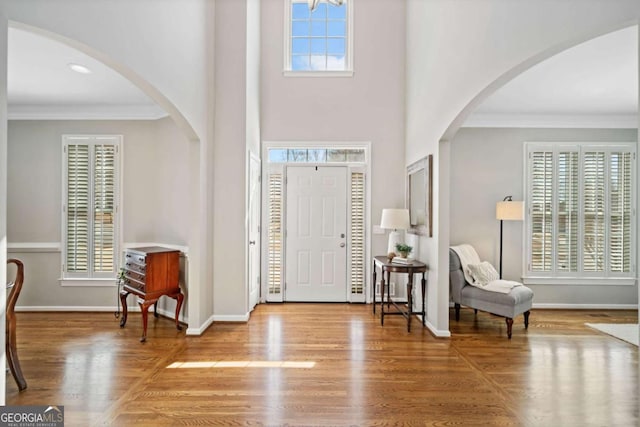 foyer entrance featuring ornamental molding, arched walkways, baseboards, and wood finished floors