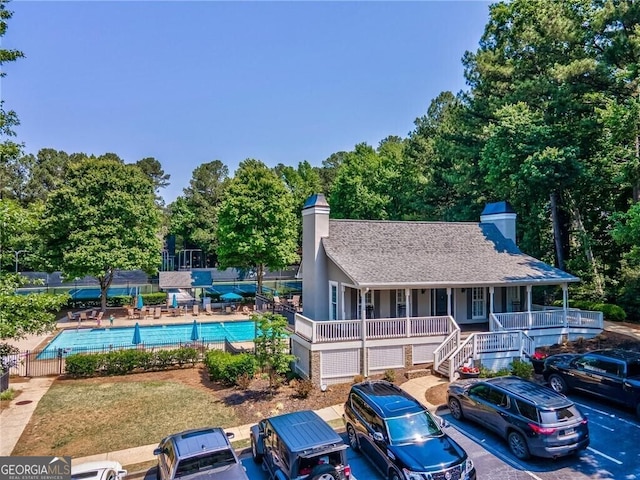 view of front facade with a shingled roof, a chimney, fence, and a community pool