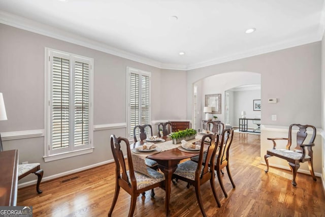 dining space with arched walkways, visible vents, baseboards, and wood finished floors