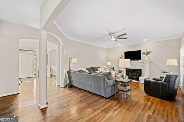 living room featuring arched walkways, ceiling fan, wood finished floors, a tile fireplace, and baseboards