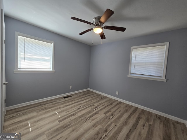 empty room with visible vents, ceiling fan, baseboards, and wood finished floors