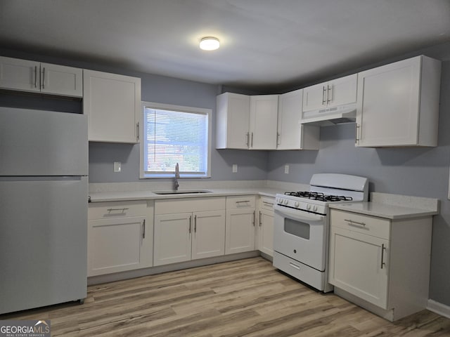 kitchen with under cabinet range hood, white range with gas stovetop, a sink, white cabinetry, and freestanding refrigerator