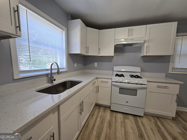 kitchen with under cabinet range hood, white range with gas stovetop, white cabinets, and a sink