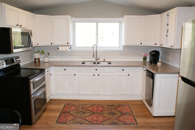 kitchen featuring light wood-type flooring, a sink, stainless steel appliances, white cabinets, and lofted ceiling