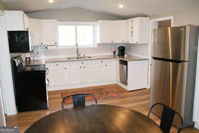 kitchen with lofted ceiling, light wood-style flooring, appliances with stainless steel finishes, white cabinets, and a sink