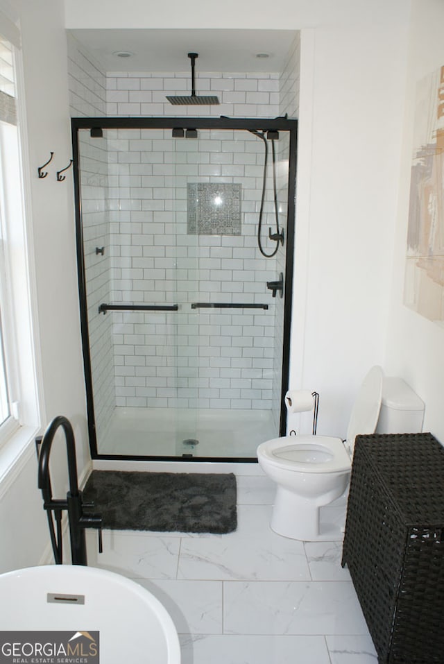 bathroom featuring toilet, marble finish floor, and a stall shower