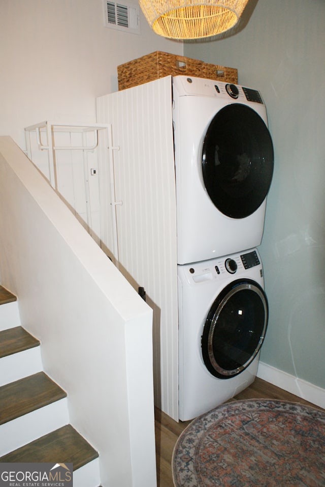 laundry area with visible vents, baseboards, laundry area, stacked washing maching and dryer, and wood finished floors