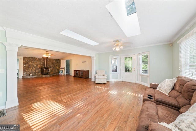 living area with a skylight, decorative columns, a ceiling fan, light wood-style flooring, and ornamental molding