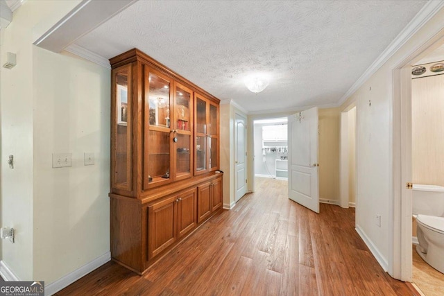 corridor with a textured ceiling, ornamental molding, wood finished floors, and baseboards