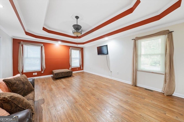 living room featuring a tray ceiling, baseboards, a healthy amount of sunlight, and light wood finished floors