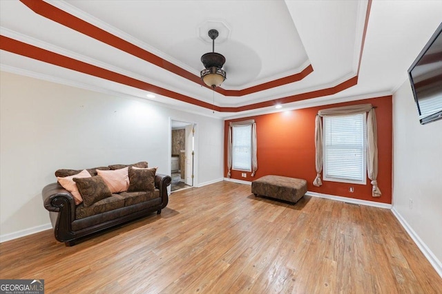 living area with ornamental molding, a raised ceiling, light wood-style flooring, and baseboards