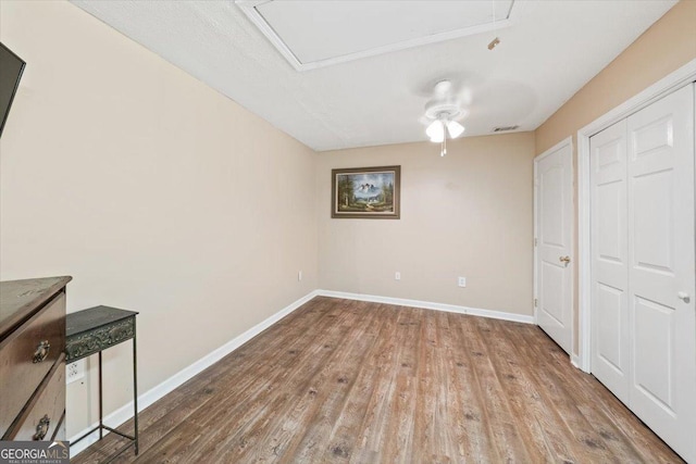 unfurnished bedroom with a closet, visible vents, attic access, wood finished floors, and baseboards