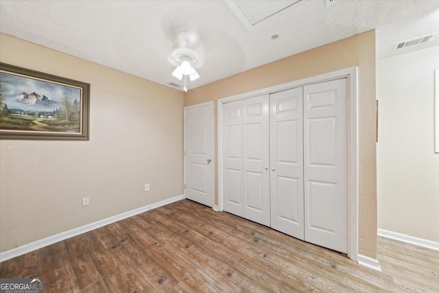 unfurnished bedroom with a closet, wood finished floors, visible vents, and baseboards