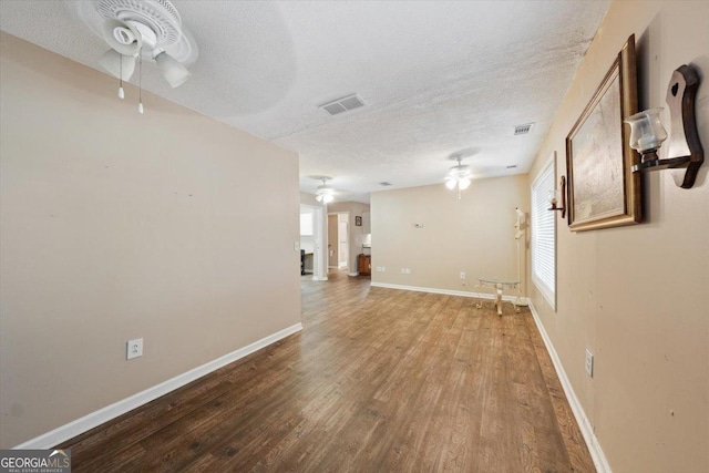 spare room with a textured ceiling, visible vents, a ceiling fan, and wood finished floors