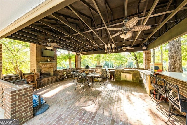 view of patio with an outdoor brick fireplace, outdoor dining area, an outdoor kitchen, and a ceiling fan