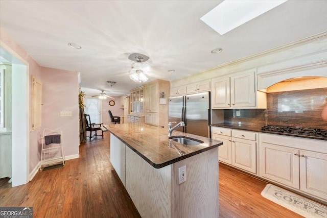 kitchen featuring a skylight, wood finished floors, a sink, appliances with stainless steel finishes, and decorative backsplash