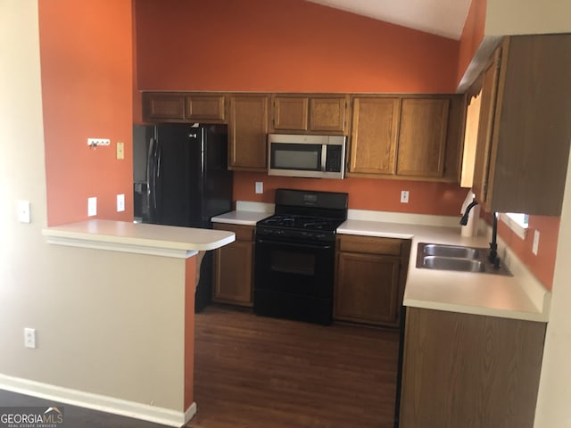 kitchen featuring light countertops, dark wood-type flooring, vaulted ceiling, a sink, and black appliances