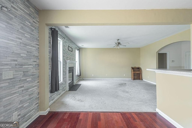 unfurnished living room with carpet floors, a ceiling fan, a large fireplace, wood finished floors, and baseboards