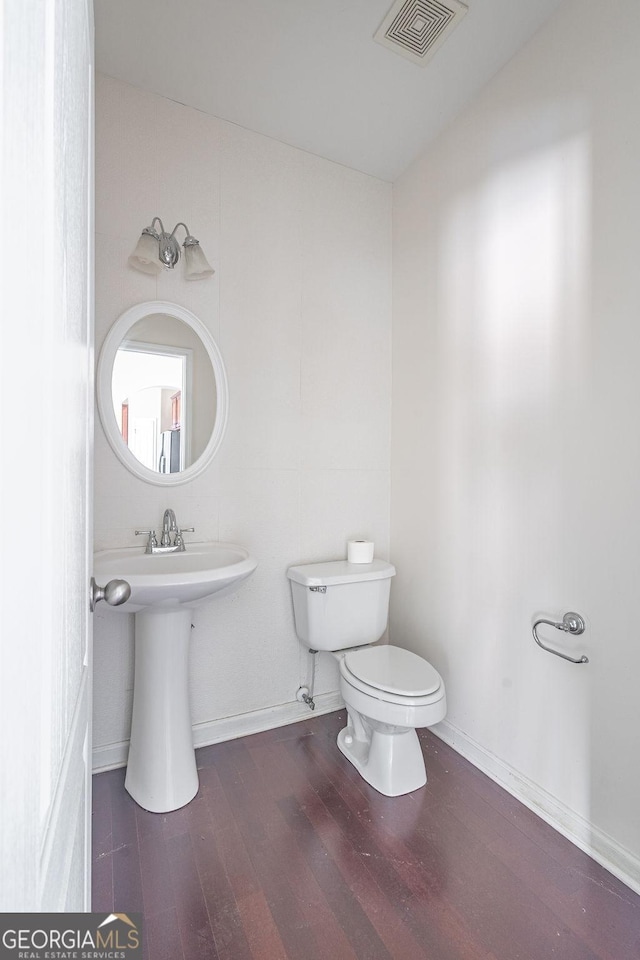 half bathroom featuring toilet, wood finished floors, visible vents, and baseboards