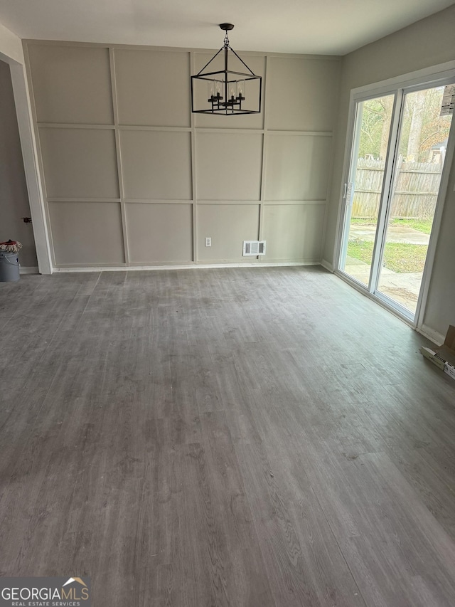 unfurnished dining area featuring wood finished floors, visible vents, and a notable chandelier