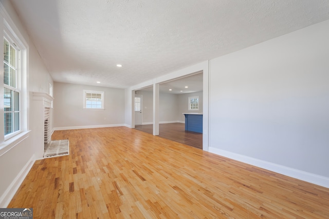 unfurnished living room featuring a textured ceiling, a fireplace, wood finished floors, and baseboards