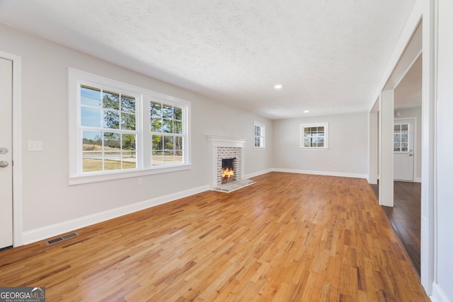 unfurnished living room featuring a brick fireplace, visible vents, light wood-style flooring, and baseboards