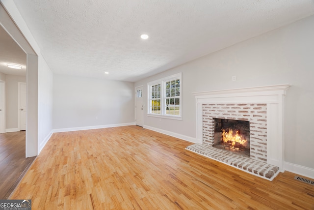 unfurnished living room with a textured ceiling, a brick fireplace, wood finished floors, and visible vents