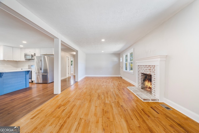 unfurnished living room featuring baseboards, visible vents, a fireplace, and light wood finished floors