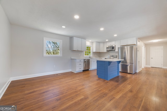 kitchen with stainless steel appliances, wood finished floors, white cabinets, light countertops, and a kitchen bar