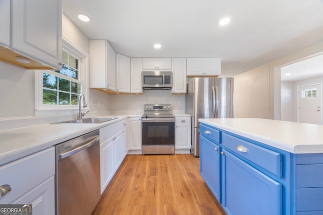 kitchen with a sink, white cabinetry, light wood-style floors, appliances with stainless steel finishes, and blue cabinetry