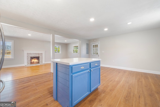 kitchen with a fireplace, light wood-style flooring, open floor plan, blue cabinets, and baseboards