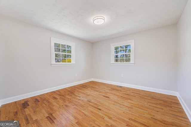 empty room with a wealth of natural light, baseboards, a textured ceiling, and light wood finished floors