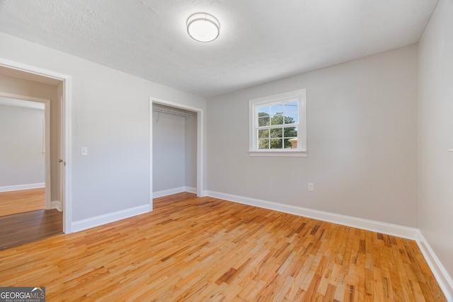 unfurnished bedroom featuring a textured ceiling, a closet, light wood-type flooring, and baseboards