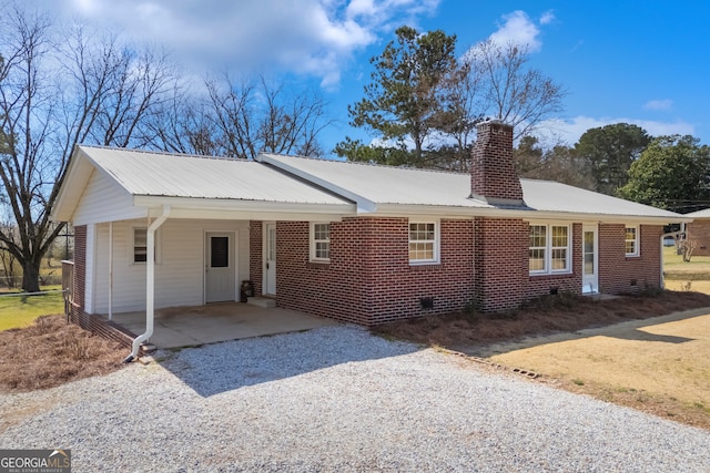 view of front facade featuring an attached carport, gravel driveway, metal roof, and a chimney