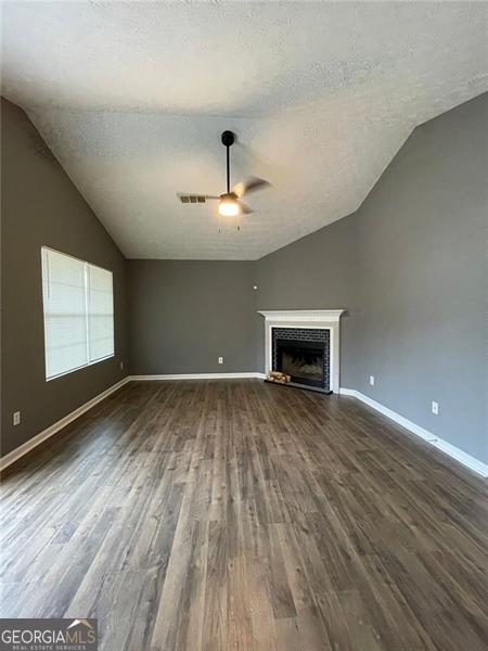 unfurnished living room with a textured ceiling, vaulted ceiling, a fireplace, and dark wood finished floors