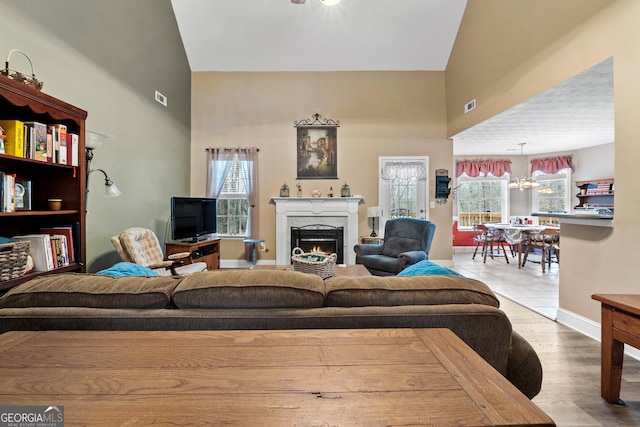 living area featuring a notable chandelier, a lit fireplace, a high ceiling, and wood finished floors