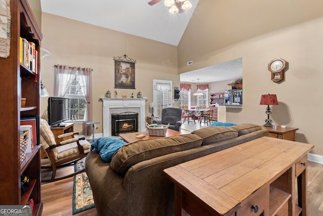 living room with a warm lit fireplace, high vaulted ceiling, wood finished floors, and a wealth of natural light